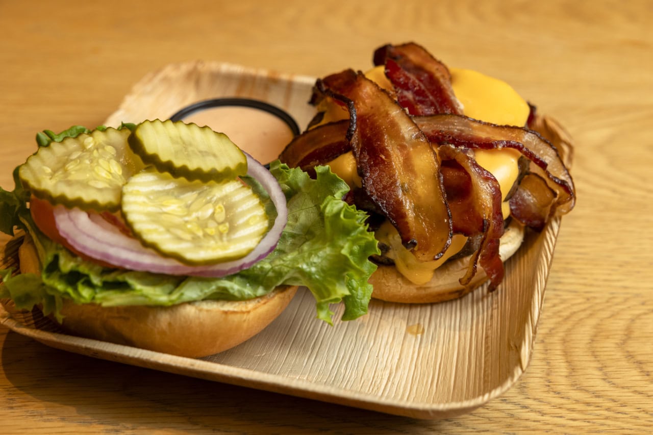 A burger topped with bacon and pickles served on a rustic wooden tray.