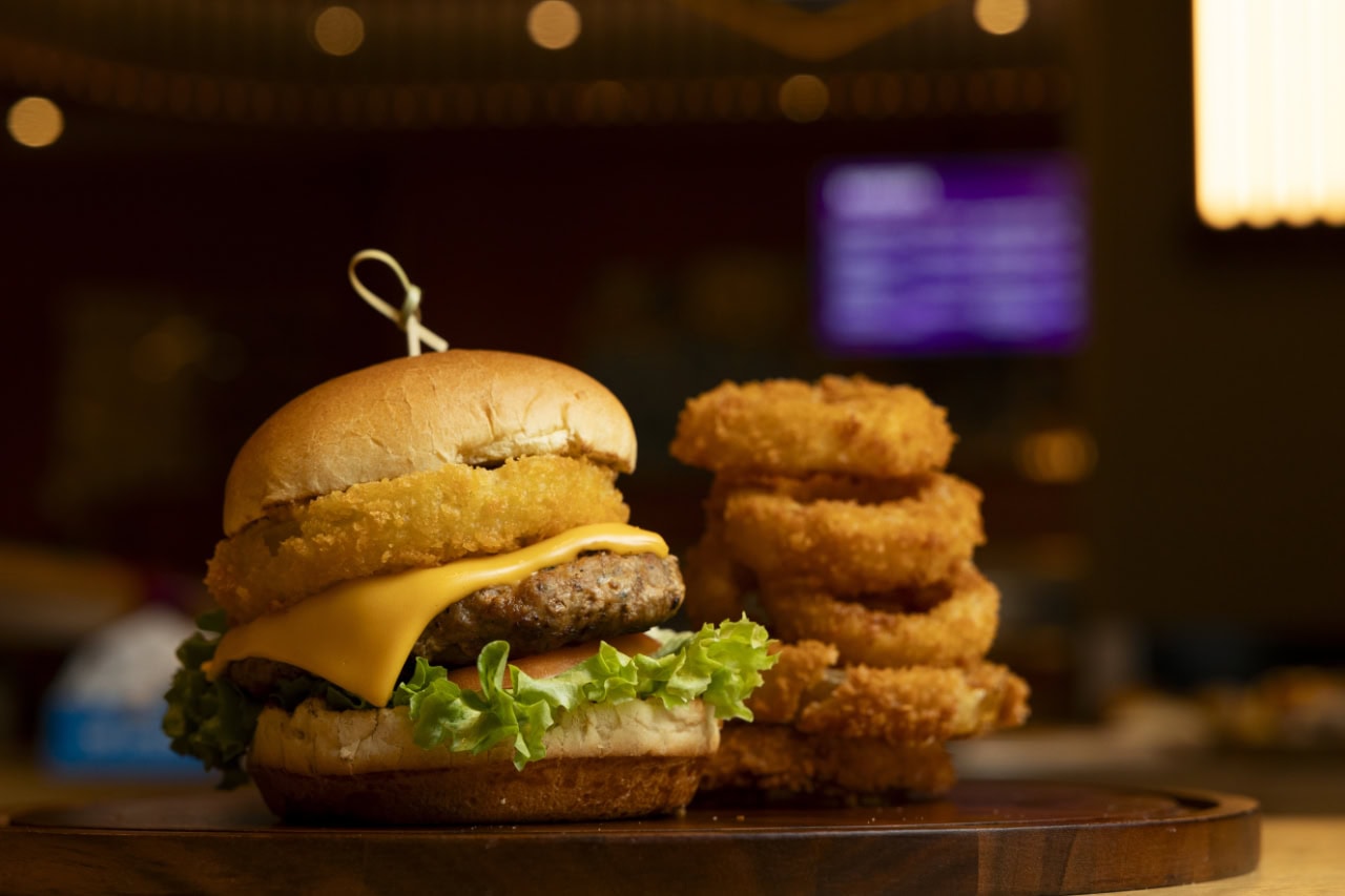 A wooden tray holds a juicy hamburger alongside crispy onion rings, creating an appetizing meal presentation.
