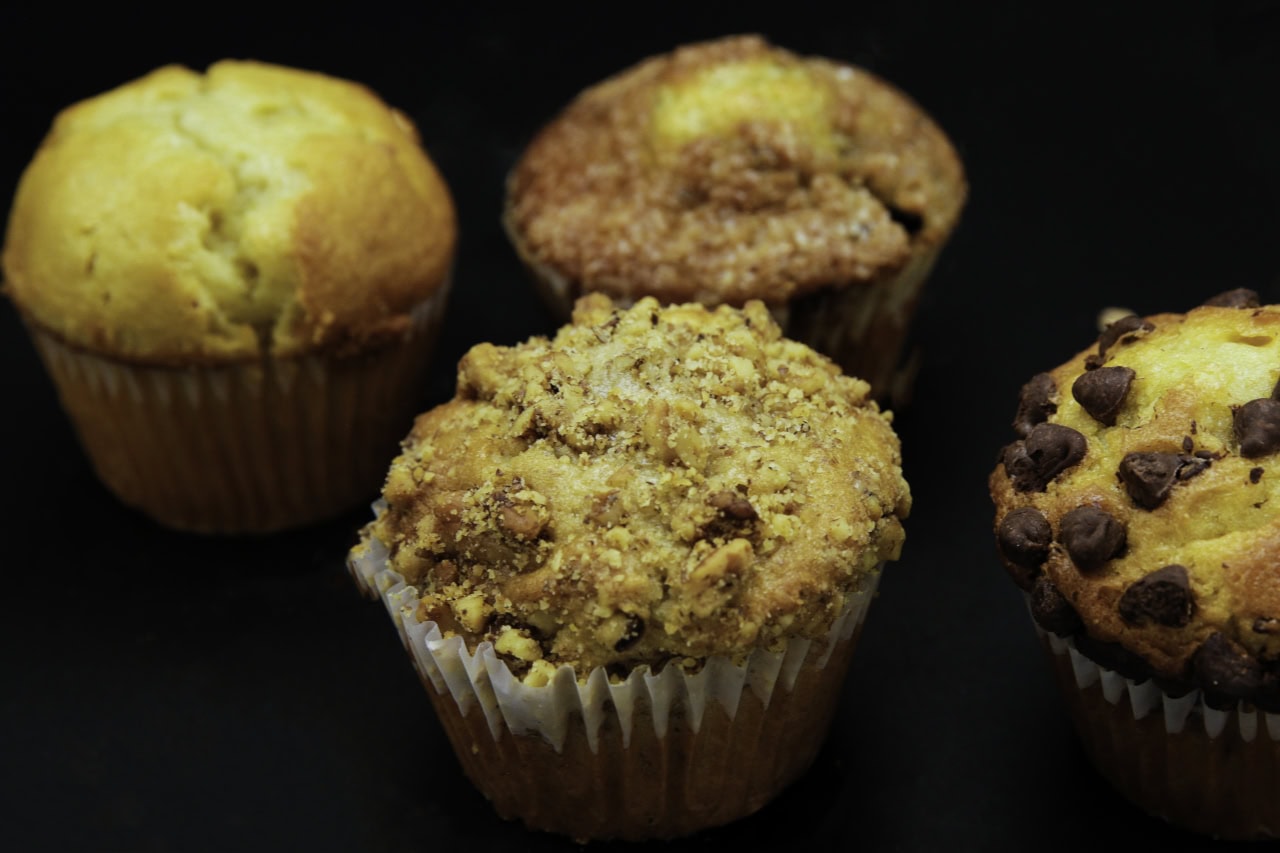 Four muffins displayed on a black surface, showcasing their golden-brown tops and textured surfaces.