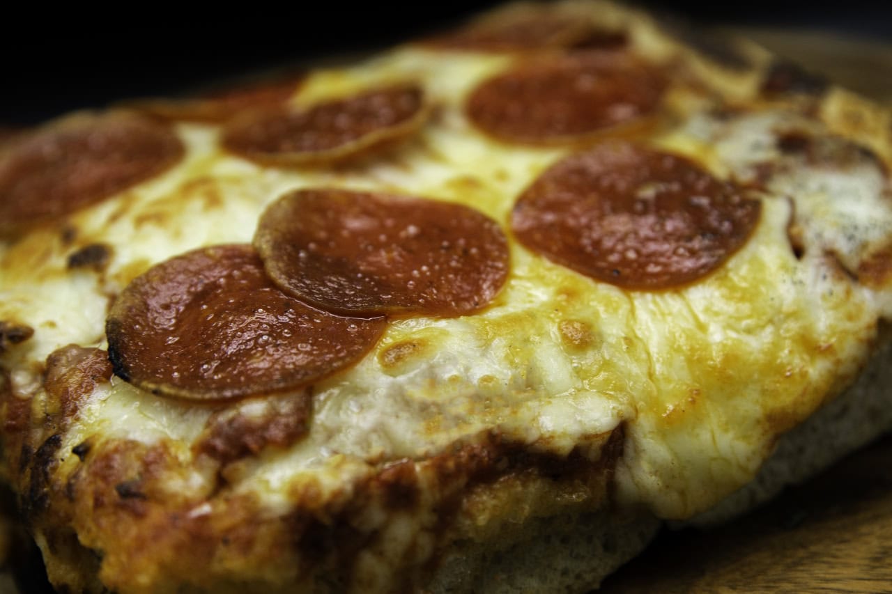 A slice of pizza resting on a rustic wooden board, showcasing melted cheese and toppings.