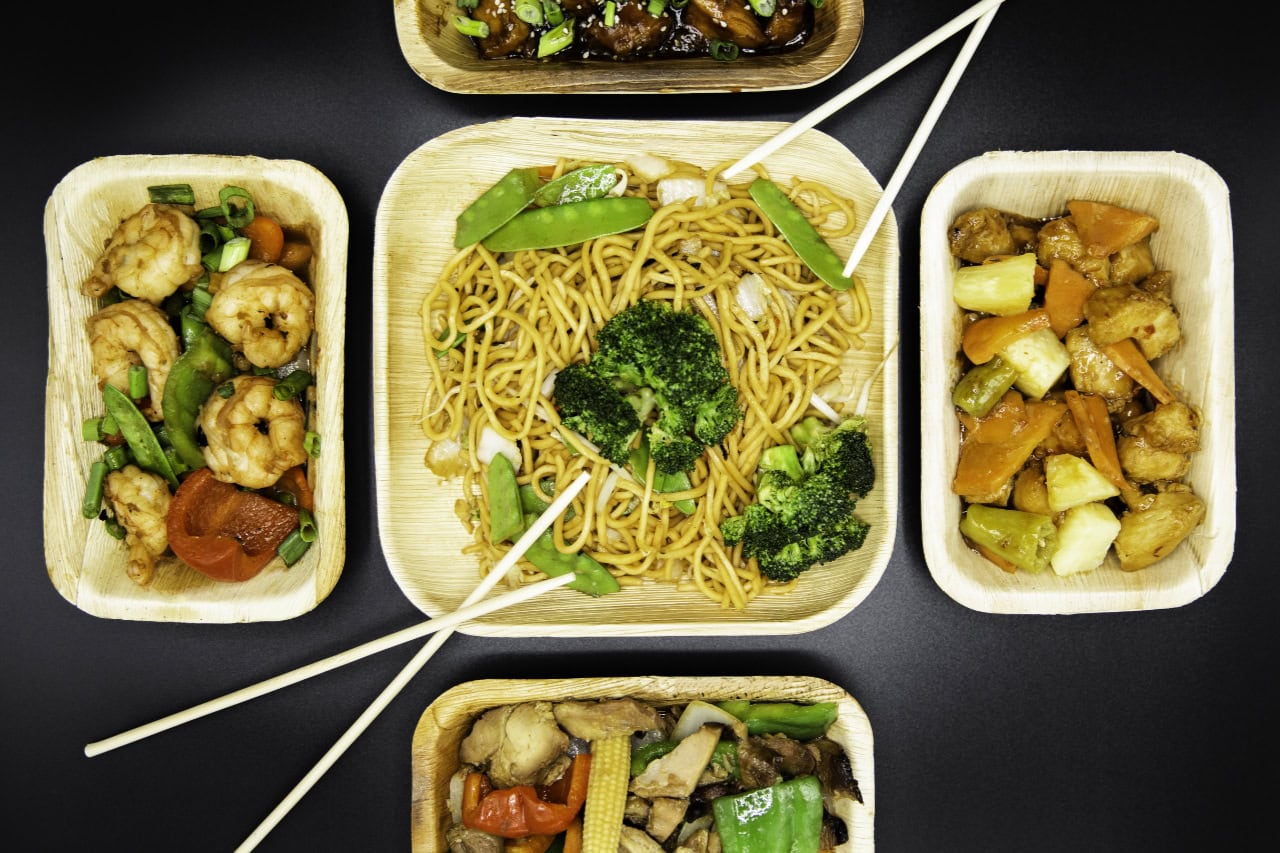 Four small food containers arranged on a table, accompanied by a pair of chopsticks resting beside them.