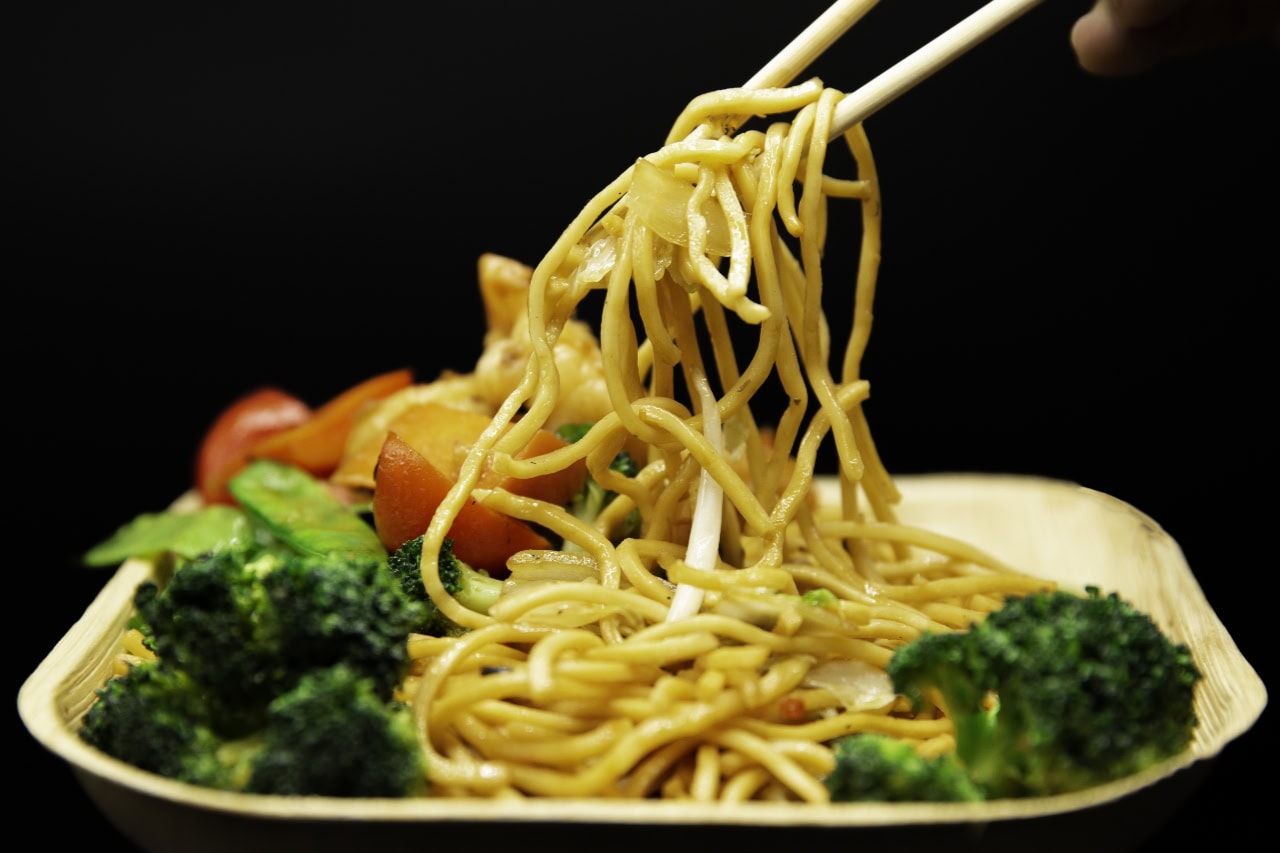 A person using chopsticks to pick up noodles from a plate.