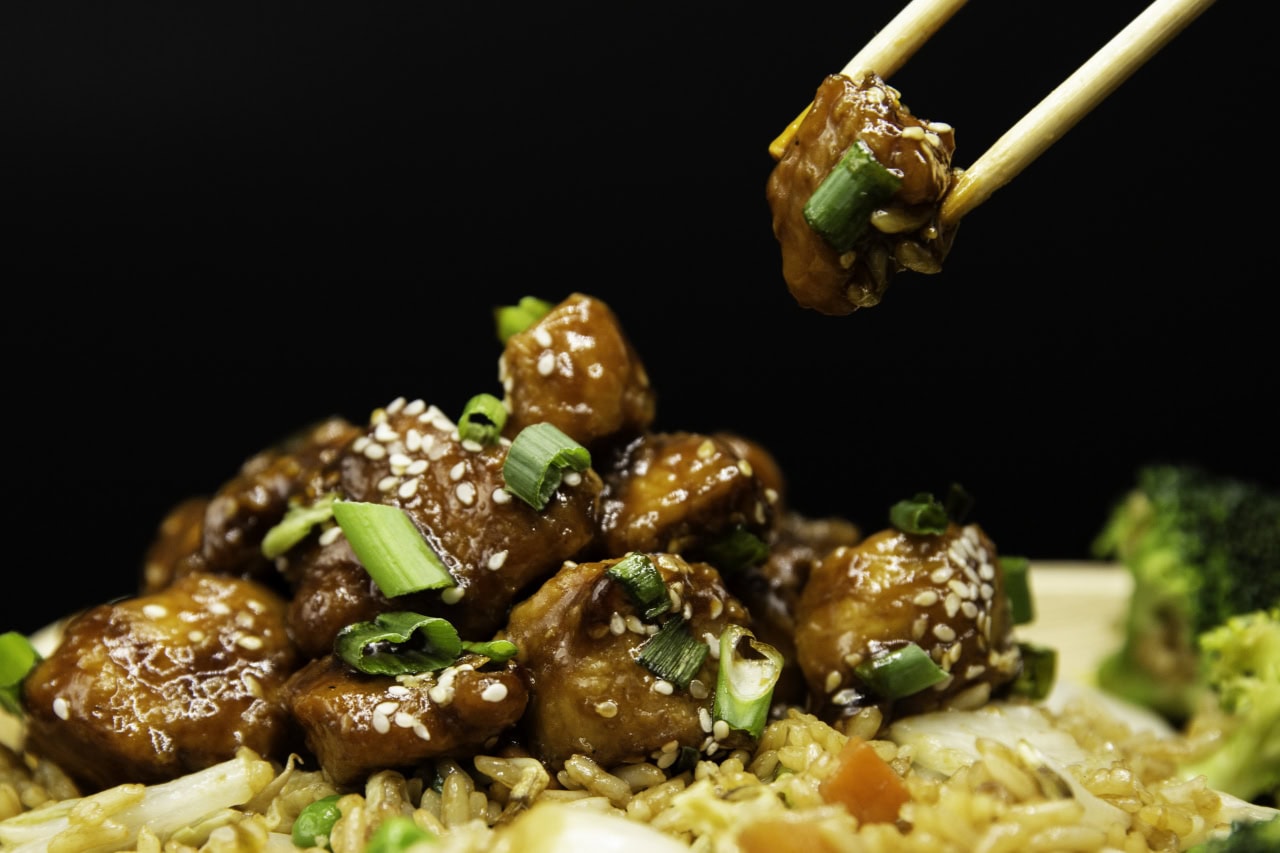Chopsticks hold a plate filled with rice and meat, showcasing a colorful and healthy meal.