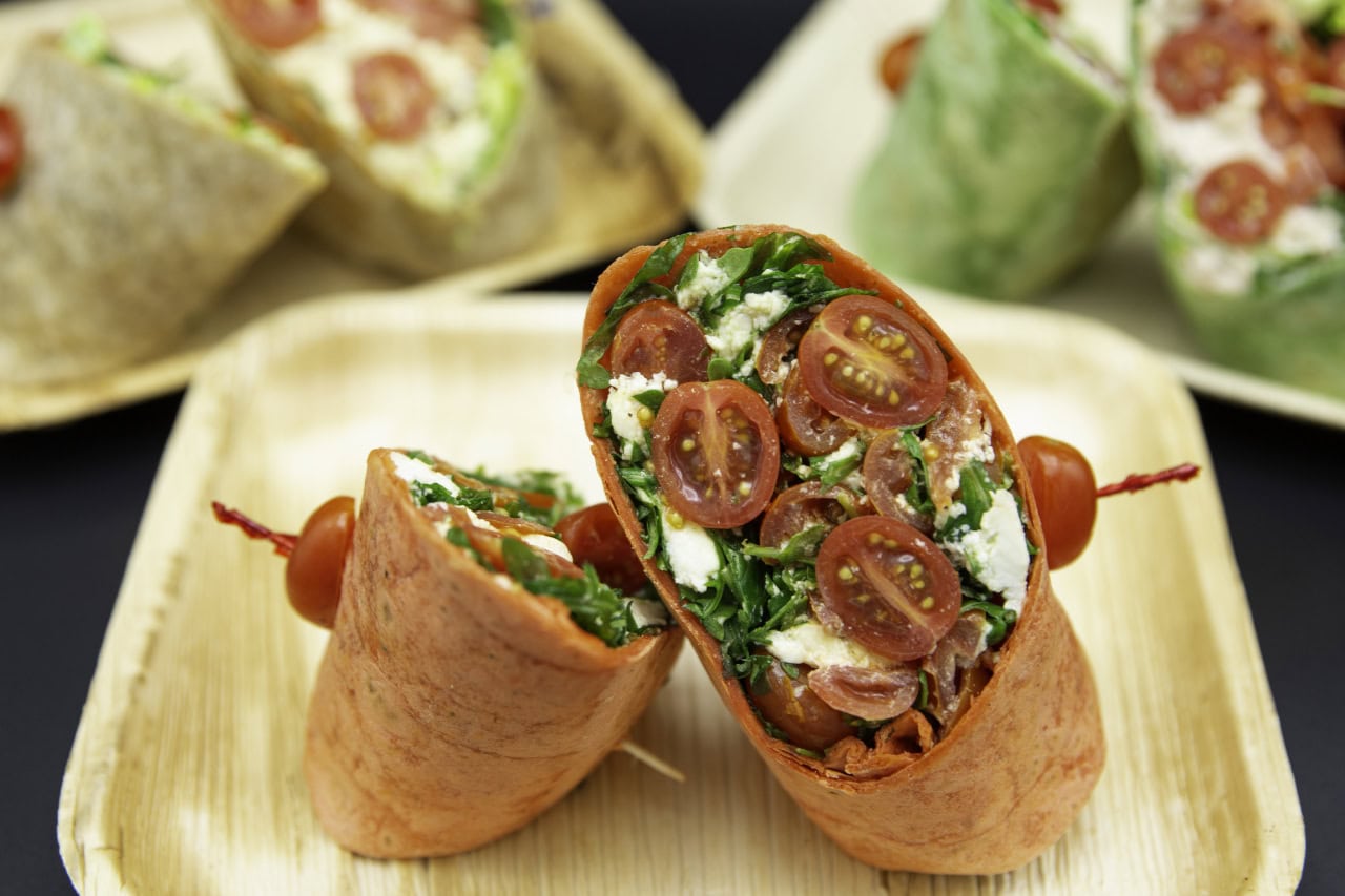 A plate featuring a wrap filled with meat, cheese, and fresh vegetables, garnished with a side of dipping sauce.